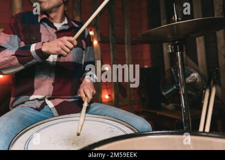 Schneide einen anonymen männlichen Musiker in lässiger Kleidung, der beim Proben auf der Bühne mit Holzstäbchen Trommeln spielt Stockfoto