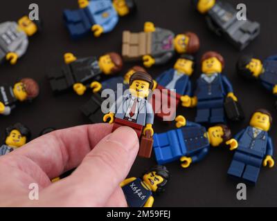 Tambov, Russische Föderation - 09. Oktober 2022 Eine Hand, die eine Lego-Geschäftsmann-Minifigure gegen einen Haufen Minifiguren hält, die auf einem schwarzen Ba liegen Stockfoto