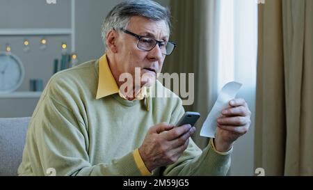 Kaukasischer 60s-jähriger älterer Geschäftsmann, Haushaltsberechnung mit Taschenrechner-App, Finanzscheck am Telefon, Geldausgabe mit Papierscheck Stockfoto