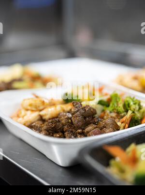 Ein vertikales Bild einer Lunchbox mit geröstetem Rindfleisch, Salat und Garnelen auf dem Tisch Stockfoto