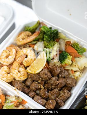 Ein vertikales Bild einer Lunchbox mit geröstetem Rindfleisch, Salat und Garnelen auf dem Tisch Stockfoto