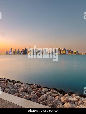 Ein Luftblick auf das Stadtbild von Doha, umgeben von Gebäuden und Wasser bei Sonnenuntergang Stockfoto