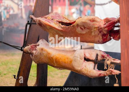 Prozess des Kochens von Schweinefleischkadavern am Spieß auf dem sommerlichen Lebensmittelmarkt Stockfoto