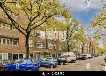 Einige Autos parkten an einer Straßenseite vor einer Reihe von Ziegelwohnungen mit gelben Blättern Stockfoto