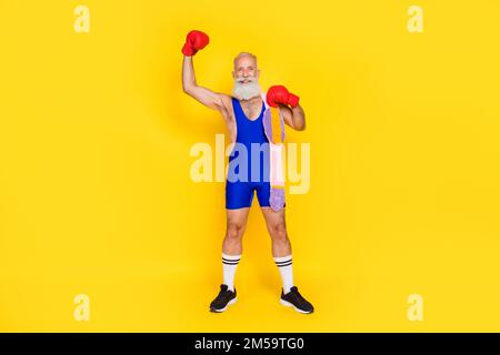 Ganzkörperfoto des gutaussehenden Großvaters Hand heben Faust Boxhandschuhe tragen Champion Gürtel isoliert auf gelbem Hintergrund Stockfoto