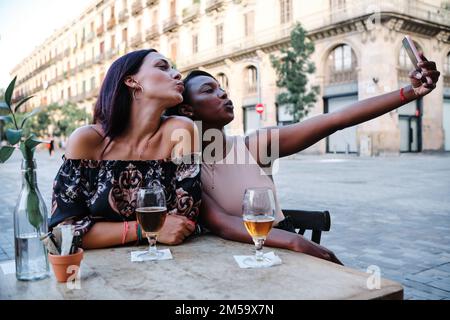 Frauen küssen sich vor der Kamera, während sie ein Selfie im Freien machen Stockfoto