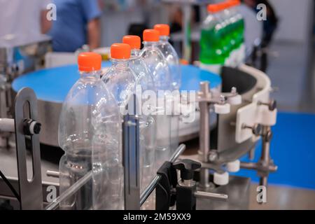 Leere PET-Limonadenflaschen mit orangefarbenen Kappen auf Förderband – Nahaufnahme Stockfoto