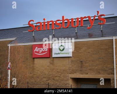 Orangefarbenes Schild auf dem Dach von Sainsburys, rot Argos und weiß Lloyds Apotheke, an der Gebäudewand Stockfoto