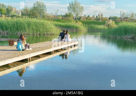 Braut und Bräutigam auf einem Ponton, der an ihrem Hochzeitstag Fotos von dem Fotografen macht, der im Hintergrund sitzt Stockfoto