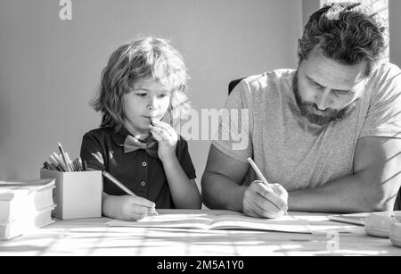 Bärtiger Vater schreibt Schulaufgaben mit seinem Jungen Sohn im Klassenzimmer, in der Schule Stockfoto