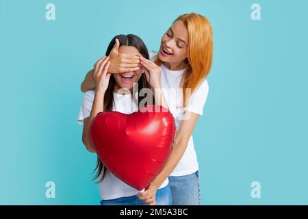 Geburtstagstag. Lächelnde Mutter und Tochter, die einen Ballon mit Liebesherz auf blauem Hintergrund halten. Alles gute zum Geburtstag meiner mutter. Stockfoto