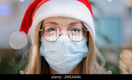 Nahaufnahme weibliches Porträt Weiße Frau weibliche Krankenschwester Arzt trägt roten Weihnachtsmann Weihnachtsmann Mütze Mütze und Brille und schützende medizinische Gesichtsmaske Neu Stockfoto