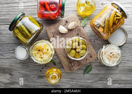 Gemüse in Dosen und eingelegtes Gemüse in Glasgefäßen auf einem Holztisch. Konservierte Speisen Stockfoto