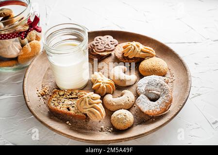 Ein Glas Milch und eine Auswahl an frischen hausgemachten Zuckerkeksen mit Butter und Nüssen Stockfoto