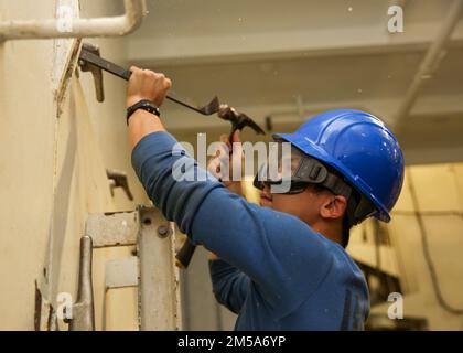 PHILIPPINE SEA (15. Februar 2022) Airman Kai Alvendia aus San Diego führt Wartungsarbeiten an einer Luke in der Hangarbucht an Bord des Flugzeugträgers USS Abraham Lincoln (CVN 72) der Nimitz-Klasse durch. Die Abraham Lincoln Strike Group befindet sich in einem geplanten Einsatz im US-7.-Flottenbereich, um die Interoperabilität durch Allianzen und Partnerschaften zu verbessern und gleichzeitig als einsatzbereite Truppe zur Unterstützung einer freien und offenen Region Indo-Pacific zu fungieren. Stockfoto