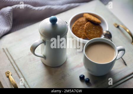 Weiße Kaffeetasse mit Keksen und Teekanne. Frühstück auf Holztisch Stockfoto