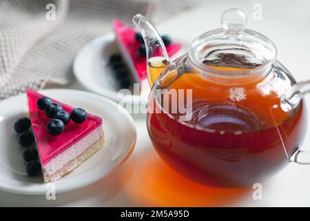 Teekanne mit heißem schwarzen Tee und Kuchen auf dem Teller mit Beeren. Nachmittagstee und süßes Sandwich Stockfoto