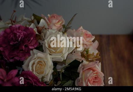 Strauß aus Rosen und Nelken in einer schwarzen Keramikvase auf weißem Hintergrund und einer Holzoberfläche Stockfoto