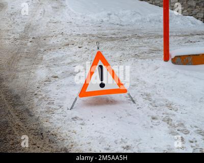 Warndreieck im schmutzigen Schnee auf einer Winterstraße. Symbol für einen Unfall auf einer rutschigen Straße. Warnsignal für andere Verkehrsteilnehmer, langsam zu tauchen. Stockfoto