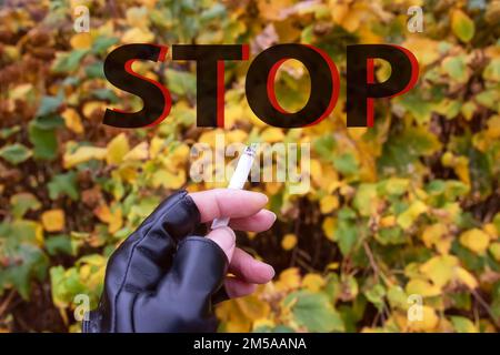 Brennende Zigarette in der Hand auf dem gelben Hintergrund lässt das Wort „Stopp“ nah heran Stockfoto