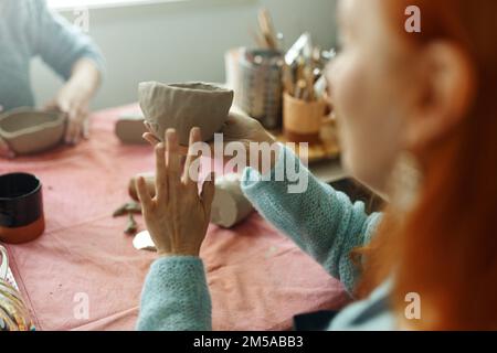 Damenhände kneten den Ton und Formen daraus eine Tasse oder Schüssel. Der Prozess der Herstellung eines keramischen Produkts Stockfoto