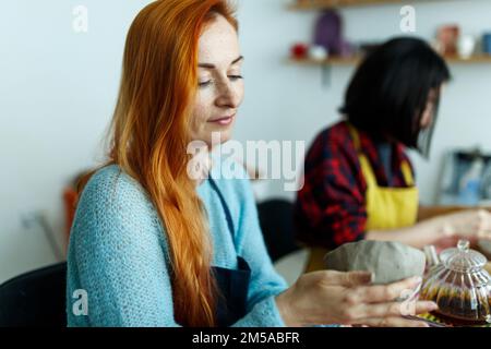 Töpferkünstlerin, die Lehm für die Formung herstellt. Nahaufnahme von Frauenhänden mit Lehm. Kreatives Handwerk. Keramikstudio Stockfoto