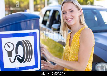 Glückliche Frau, die den Reifendruck am Auto prüft Stockfoto