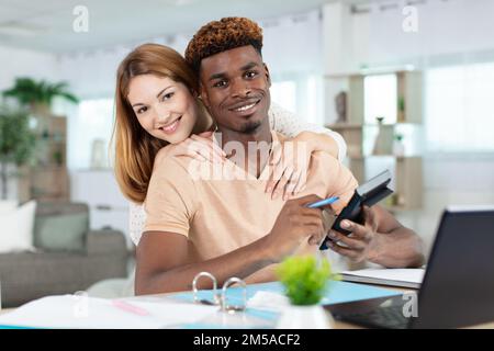 Glückliches junges glückliches Paar mit Laptop, das ein paar Berechnungen macht Stockfoto