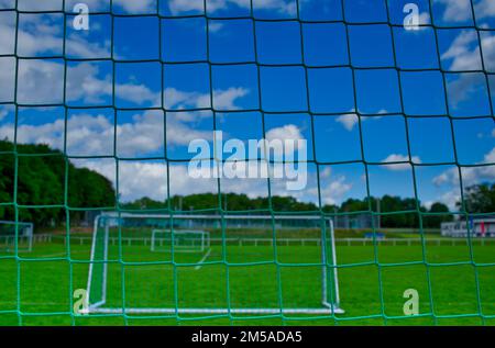 Blick durch ein Fußballzielnetz auf einem verlassenen Sportplatz mit frischem grünen Rasen und blauem Himmel (Variante B) Stockfoto