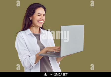 Fröhliches Lachen, junge Frau mit Laptop-Computer in der Hand schließt ihre Augen mit Lachen auf Einzelfotos. Stockfoto