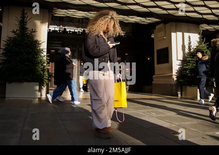 Eine Frau schaut auf ihr Handy vor dem Selfridges-Laden in der Oxford Street im Zentrum von London. Stockfoto