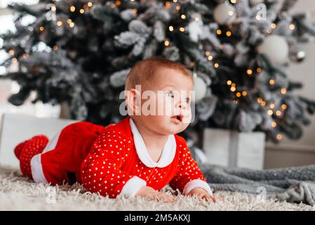 Kleines Mädchen in der Nähe des Weihnachtsbaums in einem roten Anzug Stockfoto