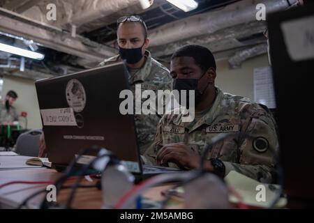 USA Air Force Senior Airman Dominique Williams, Left, ein Joint Communications Technician, der dem Joint Communications Support Element und den USA zugewiesen ist Army Staff Sgt. Cuba Zulu, Right, ein Spezialist für Brandkontrolle, arbeitet an einer Kommunikationsleitung auf der USNS-Stadt Bismarck auf der Marinebasis Guam, 16. Februar 2022. Die Dienstmitarbeiter testen Kommunikationsfähigkeiten, um die Einsatzbereitschaft zu verbessern, die gemeinsame Interoperabilität zu demonstrieren und im Pazifikraum verteilte Missionsbefehle auszuüben. Stockfoto