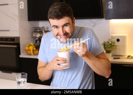 Süßer Kerl, der Instant-Nudeln in der Küche isst Stockfoto