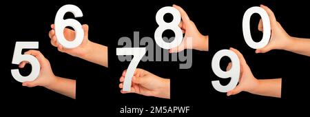 Kinderhände halten Zahlen. Ein Satz weißer Zahlen in der Hand auf schwarzem isoliertem Hintergrund. Null, fünf, sechs, sieben, acht, Neun. Stockfoto
