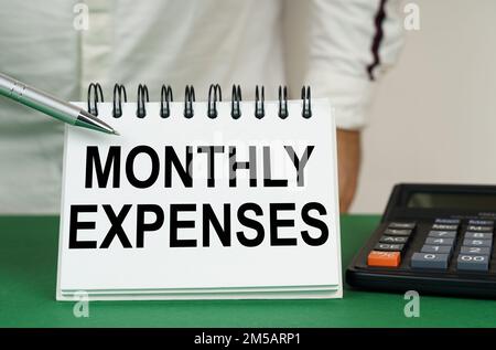 Geschäftskonzept. Auf einer grünen Oberfläche befindet sich ein Taschenrechner, ein Mann zeigt mit einem Stift auf ein Notizbuch mit der Aufschrift - monatliche Ausgaben Stockfoto