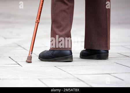 Mann mit Gehstock auf der Straße, männliche Beine in Hosen auf dem Bürgersteig. Konzept der Behinderung, hinkende Person Stockfoto