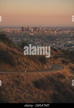 Ein Mädchen, das während des Sonnenuntergangs in Richtung einer Skyline von Los Angeles rennt Stockfoto