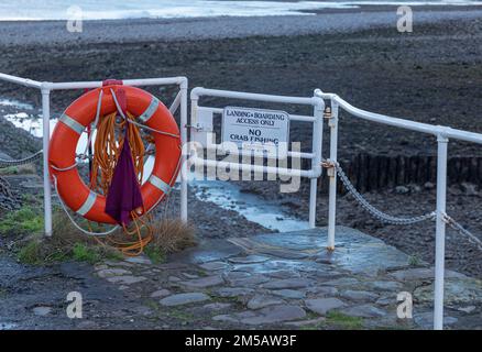 Weißer bemalter Zaun an einer Hafenmauer mit einer Rettungsboje und Hinweisschild in der Nähe Stockfoto