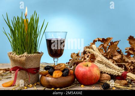 Yule log oder badnjak, Apfel, Wein, Getreide, getrocknete Früchte und eine brennende Kerze in grünem Weizen auf einem Holztisch. Konzept Feier orthodoxen Weihnachten. Stockfoto