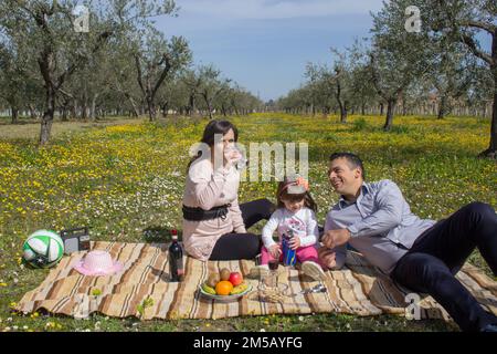 Bild einer lächelnden Familie, die auf einem Blumenfeld ein Picknick macht. Urlaub in der Toskana, Italien, Familienurlaub auf offener Landschaft. Stockfoto