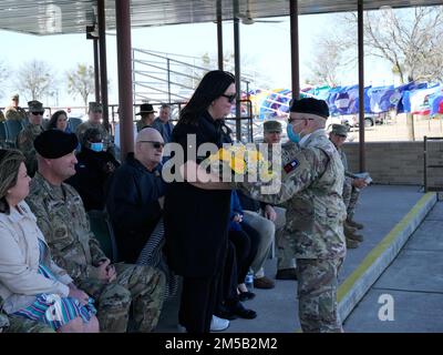 Mrs. Tina Justice (Mitte), Ehefrau von Commander Major William A. Justice (links), wird ein Strauß gelber Rosen von Sergeant 1. Class Orlando Rodriguez, Personalspezialist für Division West – First Army, Als Symbol für warme Anfänge bei einer Zeremonie zur Übernahme von Verantwortlichkeiten, die am 17. Februar 2021 auf dem Cameron Parade Field in Fort Hood, Texas, stattfindet. Stockfoto