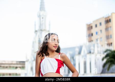 Wunderschönes Touristenmädchen an der Ortiz-Brücke mit La Ermita-Kirche im Hintergrund in der Stadt Cali in Kolumbien Stockfoto