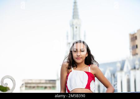 Wunderschönes Touristenmädchen an der Ortiz-Brücke mit La Ermita-Kirche im Hintergrund in der Stadt Cali in Kolumbien Stockfoto