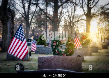 Die Sonne geht auf amerikanischen Flaggen und Weihnachtskränzen auf einem Friedhof in Wisconsin auf. Stockfoto