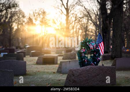 Die Sonne geht auf amerikanischen Flaggen und Weihnachtskränzen auf einem Friedhof in Wisconsin auf. Stockfoto