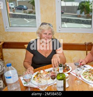 Lächelnde, süße, ältere Frau isst gerade im Resortrestaurant Teneriffa zu Abend. Stockfoto