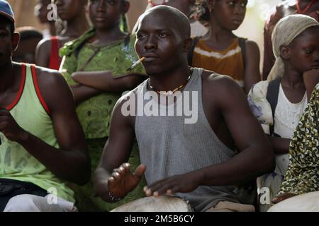 Afrikanischer Mann spielt afrikanisches Schlagzeug, während er eine Zigarette raucht. Stockfoto