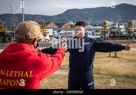 Chief Master-at-Arms Ezra Payton besprüht Hospitalman Devin Avila mit Oleoresin Capsicum (OC)-Spray während des nicht-tödlichen Waffentrainings der Hilfssicherheitskräfte (ASF) bei der CFAS am 18. Februar 2022. Das Personal der ASF nimmt an einem vierwöchigen Ausbildungslehrgang Teil, um sich während der Bedingungen für den verstärkten Schutz der Streitkräfte oder auf Anweisung des Befehlshabers der Anlage als Aufsteiger der Sicherheitskräfte der Marine einer Anlage zu qualifizieren. Stockfoto