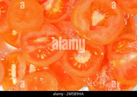Nahaufnahme frischer Tomatenscheiben auf weißem Hintergrund. Tomatenscheiben in sprudelndem Wasser auf weißem Hintergrund, Nahaufnahme. Horizontales Bild Stockfoto